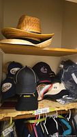 Shelf showing a stack of two straw hats on the upper shelf and a variety of ball caps below, including Coors and other brands.