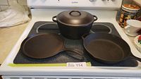 Top view of cast iron griddle, two fry pans and Dutch oven with lid on stove.