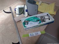Photo showing all items in the lot including the Omron blood pressure monitor with cuff, new stethoscope in box with green tubing, yellow heating pad, and white reacher/grabber tool.
