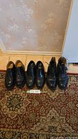 Three pairs of men's black leather shoes and boots, size 11, arranged side by side on a carpet and tile floor.