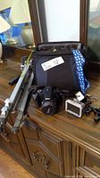Lot displayed on wooden dresser: camera bag, Nikon camera, tripod and sports camera housing