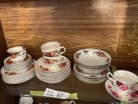 Multiple stacks of tea cups, saucers, side plates, and bowls arranged on wooden shelf, showing floral china patterns.