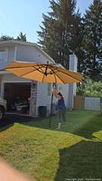 Full view of the patio umbrella setup on lawn with beige canopy and black metal frame in front of a house.