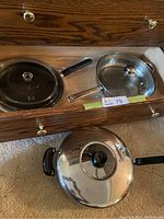 Drawer containing two large deep frypans with glass lids, one Lagostina and one stainless steel with black handle.