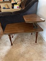 Side view of a vintage surfboard-shaped coffee table with wood grain laminate top and tapered legs next to a couch.