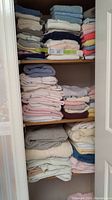 Stacked towels folded on shelves in a closet, with various pastel and neutral colors visible
