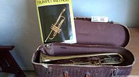 Trumpet lying in open vintage case with Trumpet Method book standing upright behind it.
