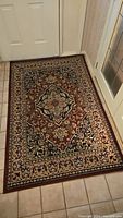 Rectangular wool floral rug in front of door on tiled floor