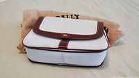 Front view of the white leather Bally purse with brown leather trim and flap closure, placed on dust cover