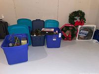 Wide shot of the plastic bins with lids containing Christmas decorations including wreaths and greenery.