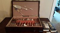 Full view of Community flatware set in open wooden case with Morton Parker napkin rings boxes beside it.