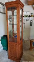 Full view of the curio cabinet showing wood finish, glass panels, and door with knob.