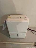 Full view of white Toshiba dehumidifier showing front water tank and top control panel area.
