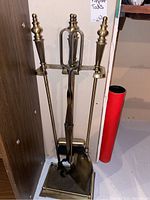 Full view of the fireplace tools hanging on the stand showing the four tools with brass handles and square base stand