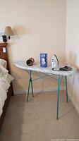 Metal ironing board with items placed on top against beige wall.