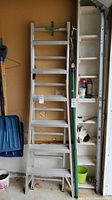 Front view of the aluminum extension ladder fully collapsed and standing upright in a garage space next to shelving and various tools.