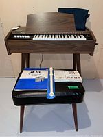 Full frontal view of the Orcana organ with matching bench, two music books and a white recorder resting on the bench seat.