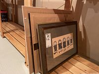 Five framed prints stacked and leaning against a wall, showing mostly the edges and back of frames, giving overall view of the lot.