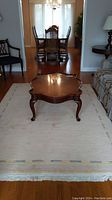 Full view of the wool rug placed under a wooden coffee table in a living/dining room area, showing overall size and condition.