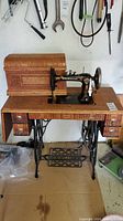 Front view of antique New Williams treadle sewing machine on wooden table with cast iron base and wooden cover case on top.