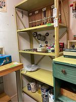 Full view of yellow metal shelving unit with three shelves containing hand tools on top two shelves and paint cans on bottom shelf.