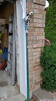 Manual tree pruner leaning against garage wall showing whole tool and pole length
