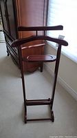 Wooden valet stand showing full front with hanger bar, small tray, and footrest bar