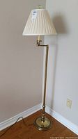 Full view of the vintage metal floor lamp with white pleated shade and brass finish standing on wood floor.