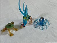 Photo showing all three Murano glass miniatures: frog, octopus, rooster on white fabric background