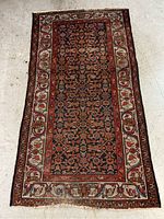 Full view of rectangular wool area rug with red and blue geometric floral pattern and multiple borders on floor.