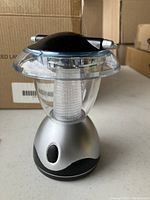 Photo of one silver mini portable LED lantern with a clear top showing the LED inside and a black on/off switch on the base.
