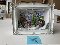 Front view of the Christmas shadow box showing ornate white frame and snowy winter village scene with animals and children.
