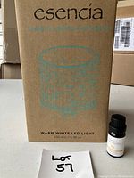 Photo of the Esencia aroma diffuser box with text indicating warm white LED light and 200 ml capacity. The lot number handwritten on a paper is also visible.