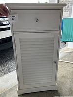 Front view of the closed white bathroom cabinet showing drawer and louvered door.
