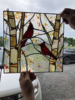Photo of stained glass panel depicting two red cardinals perched on birch tree branches with textured glass background.