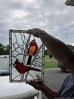 Person holding stained glass window panel with red cardinals against daylight background.