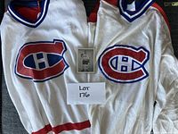 Two white Montreal Canadiens jerseys laying flat with large 'C' logo on front and a note card labeled 'LOT 176' between them.