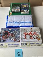 Photo of three Christmas-themed puzzles and a folded white snow blanket in packaging