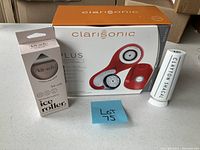 Photo of the boxed Clarisonic Plus facial and body sonics cleansing device with two interchangeable brush heads, alongside boxed Ait-schi ice roller and Clayton Shagal skincare tube.