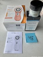 Box and user guide for Clarisonic Mia 2 device alongside a sealed jar of Skinn Cosmetics product on a white surface.