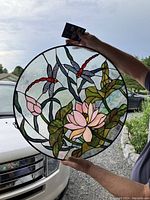 Round stained glass window panel with detailed floral and dragonfly design held up in natural light.