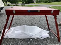 Table closed into red wooden case showing two metal latch closures and central handle on front face
