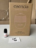 Photo of the Esencia aroma diffuser box with product name, features, and capacity visible, alongside a handwritten lot number.
