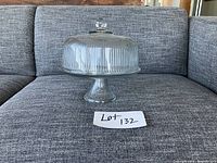 Full view of glass cake tray with domed cover on a gray couch.