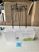Photo showing black metal wire plant stand and boxed LED desk grow light on white surface.