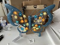 Butterfly wallhanging with illuminated small colored cube lights in yellow, blue, and orange, showing metal frame and shape.