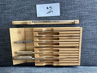 Top view of wooden kitchen knife storage rack with seven knives inserted and one sharpening steel in the rack.