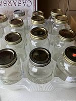 Front view of multiple clear glass pickling jars with metal lids arranged in rows in a white plastic tray.