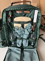 Front open view of the picnic knapsack showing wine glasses, cheese knife, corkscrew, serrated knife, and checked napkins secured inside.