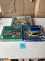 Three boxed jigsaw puzzles on a table, including Falcon de Luxe Around Britain 1000-piece, Helping Your Gardening Grow 3-in-1, and a 2000-piece night landscape puzzle.